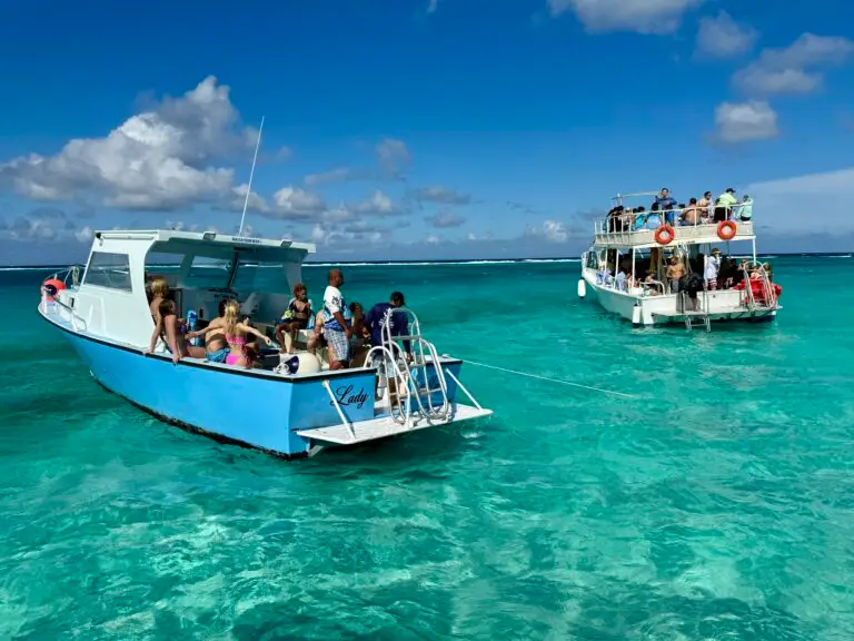 Two tour boats anchored in shallow turquoise water in the Cayman Islands, with passengers on deck