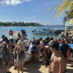 Crowds of tourists wait on a busy beach to board boats moored in turquoise water in the Dominican Republic
