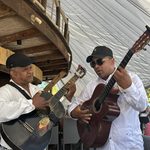 Two musicians in white shirts and caps play acoustic guitars under a white canopy at a Punta Cana restaurant