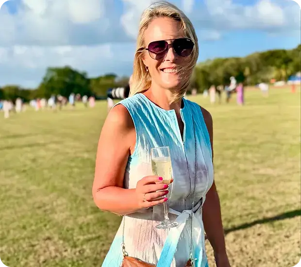 A smiling woman holding a glass of champagne on the lawn at a polo match
