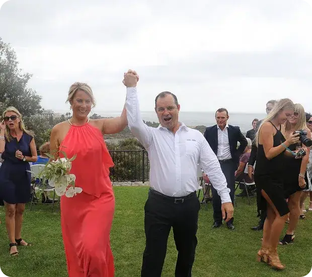 A newly married couple raising their joined hands as guests cheer at an outdoor wedding by the sea