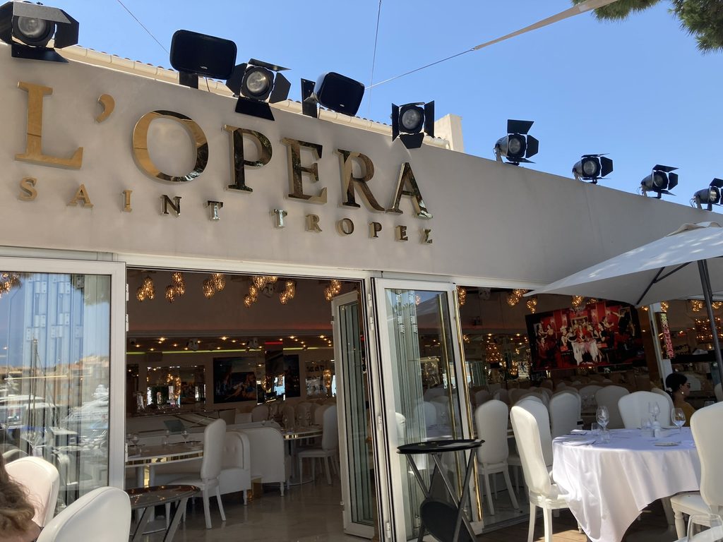L'Opera Saint Tropez restaurant entrance with gold lettering, stage spotlights and white-clothed tables