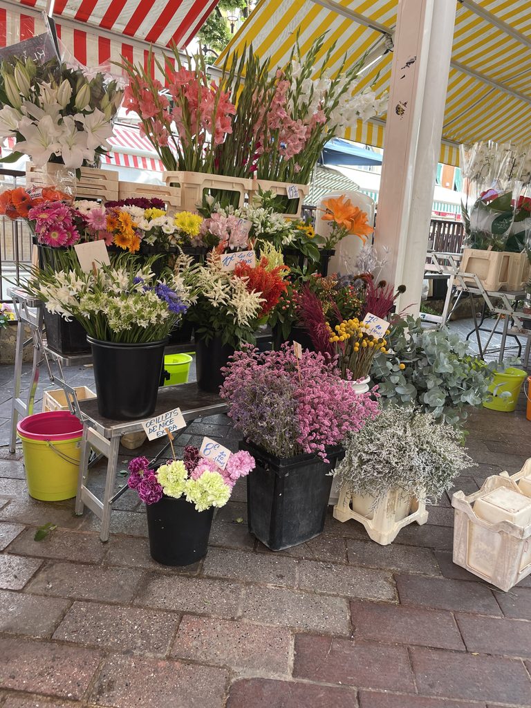 Market flower stall under striped awnings, with buckets of gladioli, lilies and colourful cut flowers
